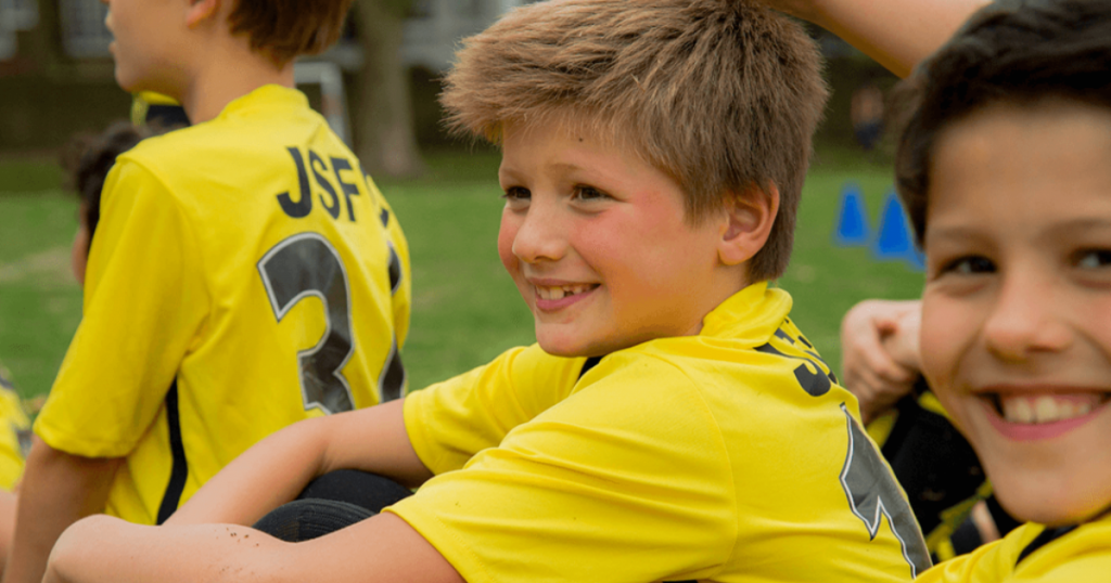 A young kid smiling during youth football development, showing how supportive environments help future football stars build confidence and love for the game.